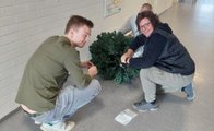 Zwei Schüler und einer Schülerin hocken im Gang der Fachschulen und bauen einen Plastikweihnachtsbaum zusammen.