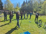 Erklärung des Bogenschießens Das Bild zeigt die Klasse dabei, wie sie einem Instruktor zusehen, der einer Schülerin den Bogen und seine Handhabung erklärt.
