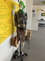 Vorbereitetes Skelett Das Bild zeigt das Skelett, das für eine Mitmachstation mit Kleidung und Schuhen, Handschuhen und einem grünen Tuch am Kopf angezogen ist.