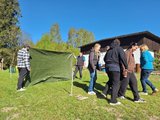 Erlebnispädagogische Übung mit einer Plane Das Bild zeigt die Gruppe des Oberkurses, die eine erlebnispädagogische Übung mit einer Plane durchführen. Dabei steht je eine Hälfte der Gruppe vor bzw. hinter der gespannten Plane.