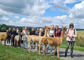 Die Schülerinnen stehen zusammen mit ihrer Lehrerin und den Alpakas, die sie zur Wanderung führen, zu einem Gruppenfoto zusammen.