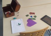 Auf dem Tisch stehen Materialien, die zum Lösen des Rätsels genutzt werden können: Eine geöffnete Schatztruhe, Puzzleteile, ein Tablet und ein Herz mit einem Hinweis.