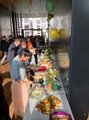 Die Gäste stehen vor einem langen Buffet-Tisch, auf dem Fingerfood ausgestellt ist.