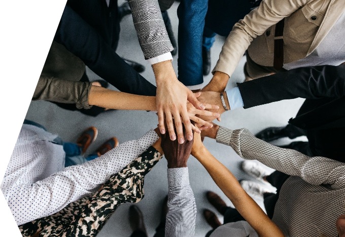 Auf dem Bild sind neun Personen von oben zu sehen, die in einem Kreis stehen und ihre Hände in der Mitte des Kreises aufeinandergelegt haben. 