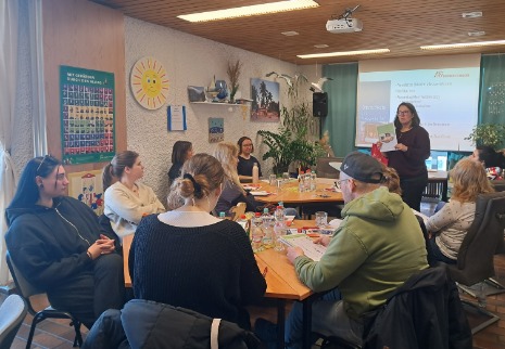 Die Schüler:innen sitzen im Gruppenraum der Offenen Behindertenarbeit Weiden und blicken zur Referentin, die gerade eine Hilfsmittel-Lupe hochhält.