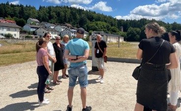 Die Schüler:innen stehen zusammen mit einem Guide im Kreis und betrachten gemeinsam eine Hinweistafel auf dem KZ-Gelände.