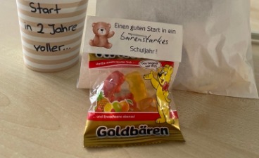 Das Bild zeigt einen Becher, der ein Schuljahr voller Inhalt wünscht, eine Schuljahresanfangstüte und ein Päckchen Gummibärchen für ein bärenstarkes Jahr.