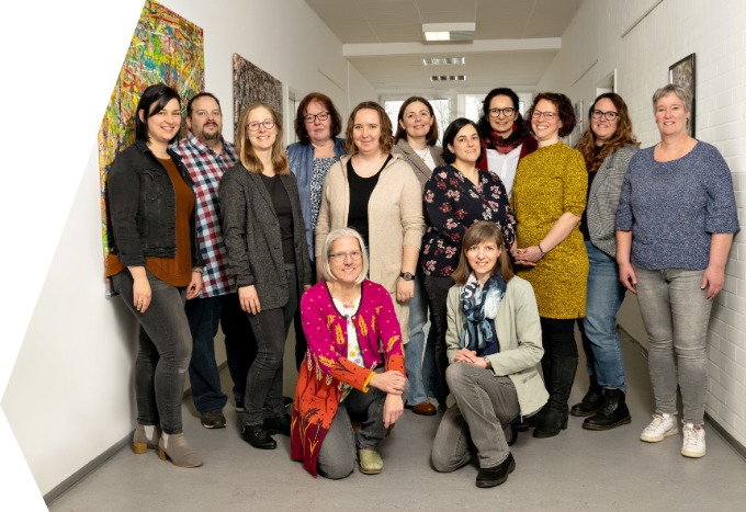 Auf dem Bild sind die Lehrkräfte der Fachschulen für Heilerziehungspflege/-hilfe zu sehen. Sie stehen im Gang des Schulgebäudes in zwei Reihen hintereinander. In einer dritten Reihe ganz vorne knien zwei Lehrerinnen.