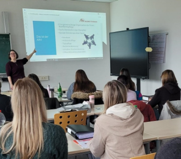 Die Leiterin des ARV steht vor der Wand und präsentiert, die Schüler*innen sitzen auf ihren Stühlen und hören zu.